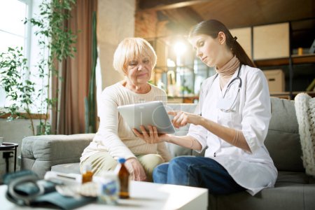 Photo for Senior woman at doctor appointment, consultation checking health in clinic, hospital on daytime. Doctor showing information on tablet. Medical care, medicine, illness, health care, profession concept - Royalty Free Image