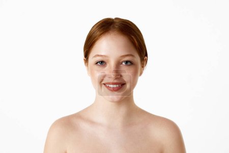Photo for Portrait of attractive, young, redhead girl with naked shoulders smiling, looking at camera over white studio background. Concept of natural beauty, plastic surgery, cosmetology, cosmetics, skin care - Royalty Free Image