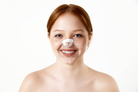 Téléchargez les photos : Portrait de jeune belle fille avec bandage sur le nez après la rhinoplastie souriant, regardant la caméra sur fond de studio blanc. Concept de beauté, chirurgie plastique, cosmétologie, santé - en image libre de droit