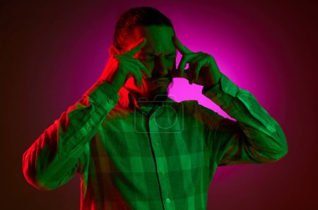 Photo for Portrait of man in checkered shirt holding head with hands, thinking against pink gradient studio background in neon light. Irritation. Concept of human emotions, facial expression, lifestyle - Royalty Free Image