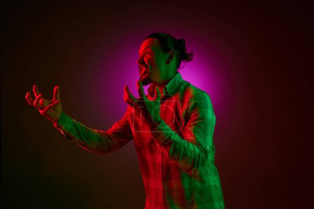 Photo for Portrait of emotional man in checkered shirt shouting in anger and irritation against dark gradient studio background in neon light. Concept of human emotions, facial expression, lifestyle - Royalty Free Image
