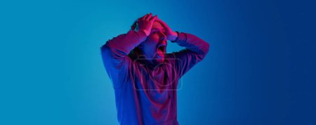 Photo for Portrait of emotional man posing with shocked, astonished face against blue studio background in neon light. Concept of human emotions, facial expression, lifestyle. Banner. Copy space for ad - Royalty Free Image