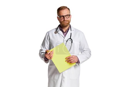 Téléchargez les photos : Portrait d'homme barbu sérieux, médecin en blouse blanche avec stéthoscope tenant des papiers médicaux sur fond blanc. Concept de médecine, de travail, de santé, de profession - en image libre de droit