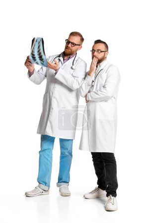 Foto de Dos hombres, doctores con bata blanca mirando la radiografía, revisando el estado de salud con fondo blanco. Cooperación. Concepto de medicina, ocupacional, salud, profesión - Imagen libre de derechos