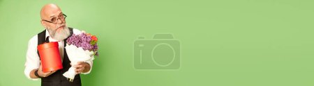 Téléchargez les photos : Portrait d'homme mûr, barbu, chauve dans des vêtements et des lunettes élégantes, debout avec des fleurs sur fond de studio vert. Concept d'émotions, mode de vie, mode, célébration. Bannière. Espace de copie pour la publicité - en image libre de droit