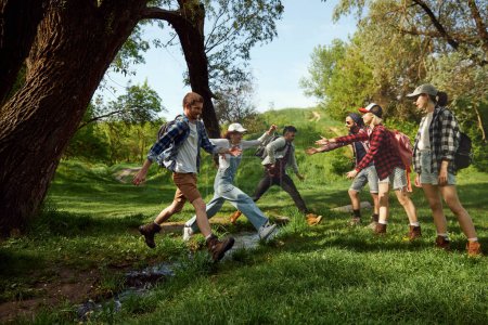 Photo for Friends, active young people going hiking, walking in forest, jumping over river on warm spring day. Active leisure time. Concept of active lifestyle, nature, sport and hobby, friendship - Royalty Free Image
