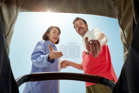 Photo for Young parents, emotional man and woman during walk on warm sunny day, looking into baby carriage with arguing faces. Concept of parenthood, family, emotions, care, happiness - Royalty Free Image