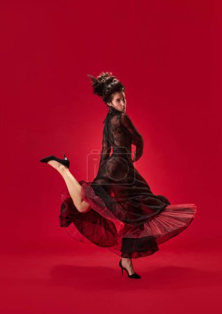 Téléchargez les photos : Portrait complet de jeune fille en élégante robe noire dansant sur fond rouge. Passion et beauté. Concept d'histoire, art de la renaissance, comparaison des époques - en image libre de droit