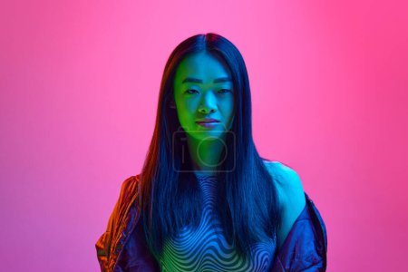 Photo for Portrait of young korean girl looking at camera with little smile, posing against pink studio background in neon light. Concept of emotions, facial expression, youth, lifestyle, inspiration, sales, ad - Royalty Free Image