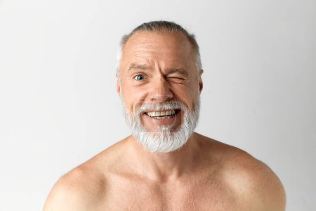 Téléchargez les photos : Portrait d'un homme d'âge moyen, mature, beau, barbu, souriant à moitié nu, regardant la caméra sur fond gris. Concept de beauté masculine, soins du visage et de la peau, procédures quotidiennes, âge - en image libre de droit