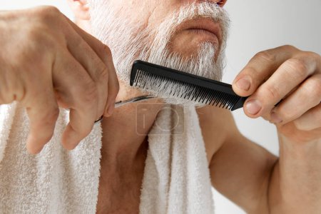 Photo for Barber. Cropped image of mature mans face, male model taking care after face, cutting and brushing beard against grey background. Concept of male beauty, face and skin care, daily procedures, age - Royalty Free Image