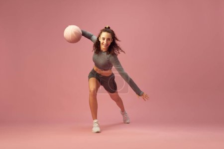 Téléchargez les photos : Jeune fille souriante en tenue de sport grise, ballon de basket-ball dribble sur fond de studio rose. Image dynamique. Concept de style de vie sportif, beauté, soins du corps, fitness, santé - en image libre de droit