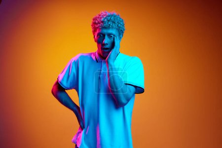 Photo for Portrait of mature man with wide open eyes expressing shock and surprise against orange studio background in blue neon light. Concept of human emotions, lifestyle, youth, facial expression - Royalty Free Image