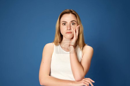 Photo for Portrait of young girl in casual clothes showing emotion of shock against blue studio background. Astonishment and surprise. Concept of youth, human emotions, facial expression, sales, business - Royalty Free Image