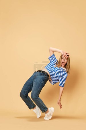 Foto de Retrato de larga duración de una joven rubia en camiseta a rayas y jeans, posando sobre fondo amarillo del estudio. Estudiante. Concepto de juventud, emociones humanas, expresión facial - Imagen libre de derechos