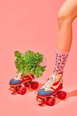 Foto de Pierna femenina en rodillos vintage y divertidos calcetines con lechuga sobre fondo rosa. Nutrición, alimentación saludable, dieta. Concepto de fotografía pop art, visión creativa, imaginación. Arte mínimo - Imagen libre de derechos