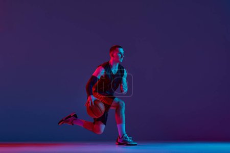 Photo for Concentrated young man, basketball player during game, training, dribbling ball against purple studio background in neon light. Concept of professional sport, hobby, healthy lifestyle, action, motion - Royalty Free Image