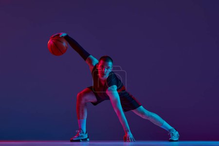 Photo for Concentration and motivation. Young man, basketball player in motion with ball against purple studio background in neon light. Concept of professional sport, hobby, healthy lifestyle, action, game - Royalty Free Image