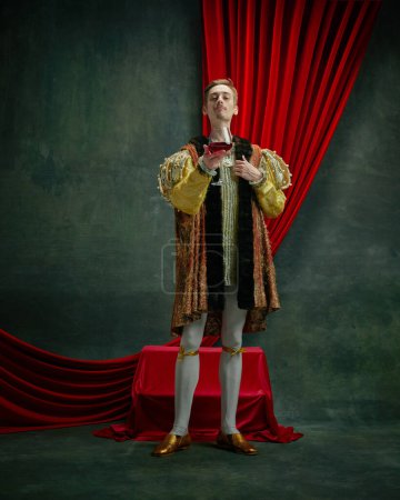 Photo for Portrait of young duke, prince, royal person in vintage costume raising glass of red wine against dark green, vintage background. Concept of comparison of eras, history, renaissance art, remake - Royalty Free Image