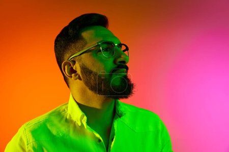 Photo for Handsome bearded man in glasses and white shirt posing with confident, serious face against gradient studio background in neon light. Concept of human emotions, facial expression, lifestyle, business - Royalty Free Image