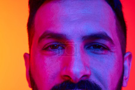 Photo for Close-up cropped image of male eyes looking with calmness and attention against gradient red orange studio background in neon light. Concept of human emotions, facial expression, lifestyle - Royalty Free Image