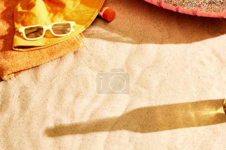 Téléchargez les photos : Ombre de bouteille de bière sur sable chaud avec des étoffes de plage. Refroidir la plage par une chaude journée d'été avec boisson fraîche. Concept de boisson alcoolisée, goût, vacances d'été, vacances, brasserie. Publicité - en image libre de droit
