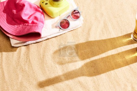 Foto de Sombra de vaso de cerveza y botella en arena caliente con productos de playa. Playa chill en el cálido día de verano con bebida fresca. Concepto de bebida alcohólica, sabor, vacaciones de verano, vacaciones, cervecería. Publicidad - Imagen libre de derechos
