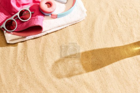 Téléchargez les photos : Ombre de verre à bière sur sable chaud avec des étoffes de plage. Refroidir la plage par une chaude journée d'été avec boisson fraîche. Concept de boisson alcoolisée, goût, vacances d'été, vacances, brasserie. Publicité - en image libre de droit