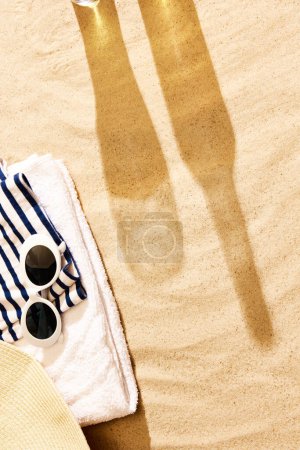 Téléchargez les photos : Ombre de verre à bière et bouteille sur sable chaud avec des étoffes de plage. Refroidissement par une chaude journée d'été avec une boisson fraîche. Concept de boisson alcoolisée, goût, vacances d'été, vacances, brasserie. Publicité - en image libre de droit