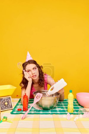 Photo for Bored, pretty young woman with dirty face with flour cooking cake for her birthday party against vivid yellow background. Concept of party, celebration, emotions, female beauty, youth. Pop art - Royalty Free Image