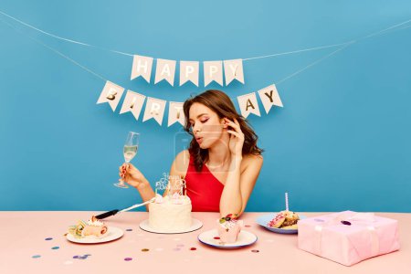 Téléchargez les photos : Jolie jeune fille célébrant son anniversaire, buvant du champagne, mangeant du gâteau et faisant des vœux sur fond bleu. Concept de fête, célébration, émotions, beauté féminine, jeunesse. Pop art - en image libre de droit