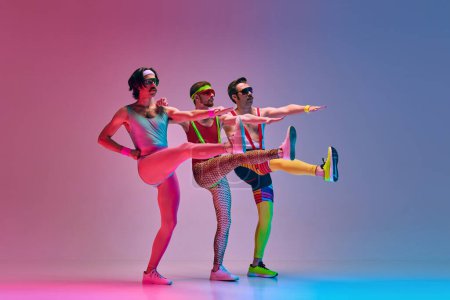 Photo for Three men in vintage, funny, colorful sportswear training, stretching against gradient blue pink studio background. Aerobics. Concept of sportive and active lifestyle, humor, retro style. Ad - Royalty Free Image