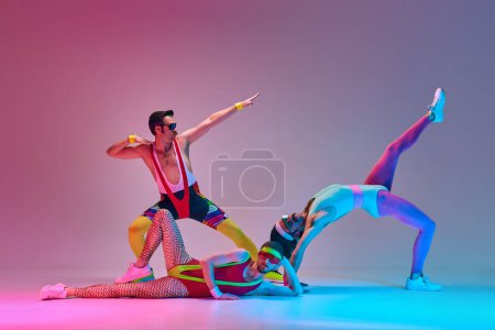 Foto de Los jóvenes, los hombres en colorido entrenamiento ropa deportiva retro contra degradado azul rosa fondo del estudio en luz de neón. Concepto de estilo de vida deportivo y activo, humor, estilo retro. Anuncio - Imagen libre de derechos