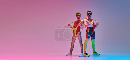 Stylische junge Männer in farbenfroher Retro-Sportbekleidung posieren über gradienten blaurosa Studiohintergrund in Neonlicht. Konzept des sportlichen und aktiven Lebensstils, Humor, Retro-Stil. Banner. Kopierraum für Werbung