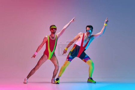 Photo for Young men, fitness coach in colorful sportswear stretching, training against gradient blue pink studio background in neon light. Concept of sportive and active lifestyle, humor, retro style. Ad - Royalty Free Image