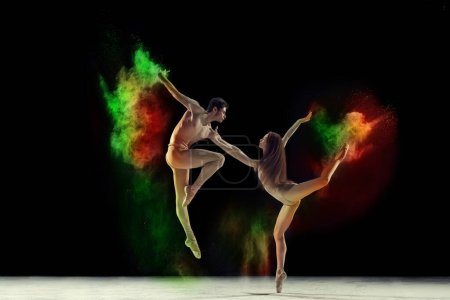 Foto de Hermoso joven y mujer, talentosos bailarines de ballet en trajes de cuerpo beige bailando con colorida explosión de polvo sobre fondo negro. Concepto de arte, festival, belleza de la danza, inspiración, juventud - Imagen libre de derechos