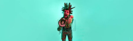 Photo for Young expressive shirtless man, punk shouting in megaphone with aggression over blue background in neon light. Concept of music, lifestyle, subculture, art, youth, emotions. Banner. Copy space for ad - Royalty Free Image
