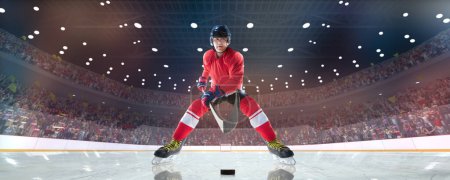 Foto de Hombre, jugador de hockey profesional en uniforme, casco de pie en 3D pista de hielo arena con palo y disco durante el partido. Público borroso. Concepto de deporte, competición, partido, juego, acción y movimiento - Imagen libre de derechos