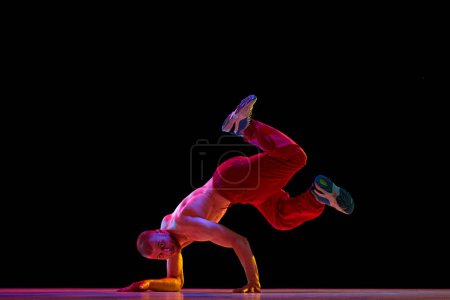 Téléchargez les photos : Musclé, torse nu, jeune homme dansant hip-hop, breakdance sur fond de studio noir. Performance moderne. Concept d'art, danse de rue, mode, jeunesse, passe-temps, dynamique, publicité - en image libre de droit