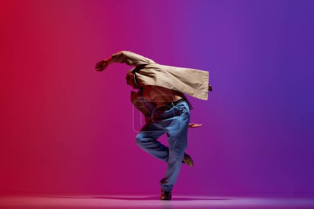 Foto de Joven hombre deportivo, en ropa casual elegante baile breakdance, hip-hop sobre fondo rosa púrpura estudio. Cuerpo muscular. Concepto de arte, danza de estilo callejero, moda, juventud, hobby, dinámica, anuncio - Imagen libre de derechos