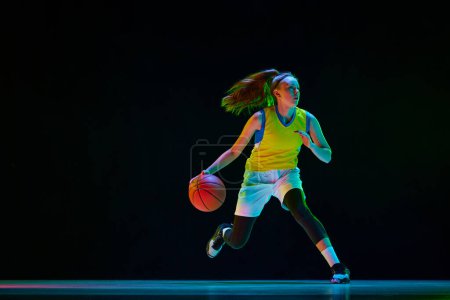 Photo for Young motivated girl, basketball player in uniform running with ball against black studio background in neon light. Concept of professional sport, action and motion, game, competition, hobby, ad - Royalty Free Image