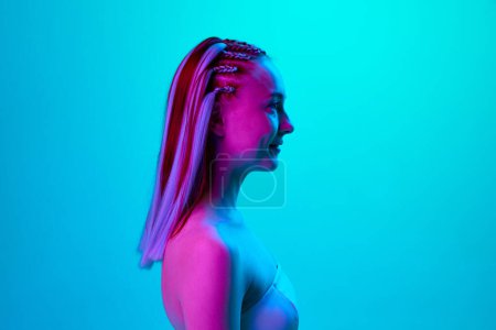 Photo for Profile portrait of young pretty girl with cute hairstyle posing, looking straight against blue studio background in neon light. Concept of youth, emotions, beauty, lifestyle, ad - Royalty Free Image