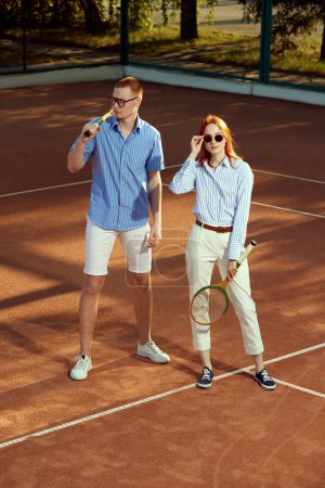 Photo for Portrait of stylish, beautiful young man and woman in casual clothes posing on opendoor tennis court on warm sunny day. Top view. Concept of sport, active lifestyle, hobby, fashion, leisure, ad - Royalty Free Image