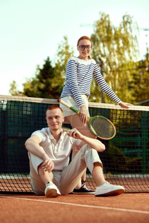 Photo for Full-length image of beautiful young woman and handsome man in casual, stylish clothes posing on tennis court on daytime. Concept of casual fashion, sport, active lifestyle, hobby, leisure time, ad - Royalty Free Image