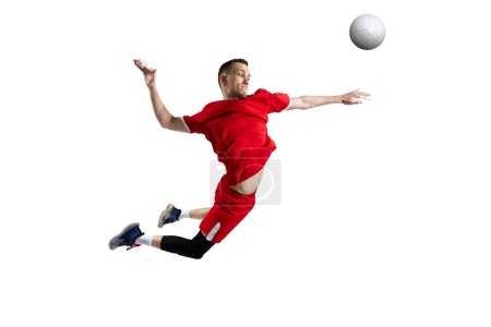 Téléchargez les photos : Jeune homme, athlète professionnel en uniforme rouge en mouvement, frappant la balle en saut, jouant au volley-ball sur fond de studio blanc. Concept de sport, mode de vie actif, santé, dynamique, jeu, publicité - en image libre de droit