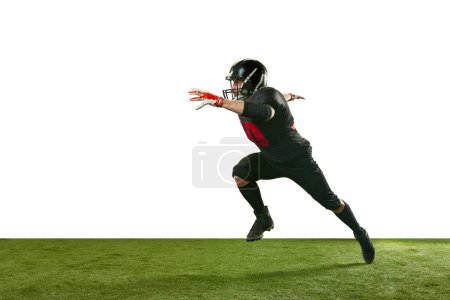 Foto de Imagen dinámica del hombre en uniforme negro y casco, jugador de fútbol americano en movimiento, corriendo en el campo sobre fondo blanco. Deporte profesional, acción, estilo de vida, competencia, entrenamiento, concepto de anuncio - Imagen libre de derechos