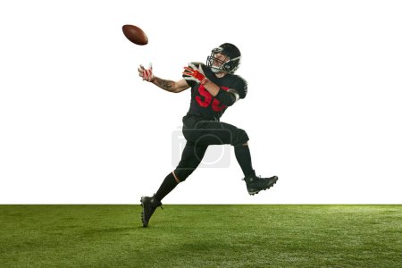 Photo for Concentrated man, american football player in black uniform in motion, running and catching ball against white background. Concept of professional sport, action, lifestyle, competition, training, ad - Royalty Free Image