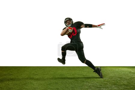 Foto de Hombre, jugador de fútbol americano en uniforme negro atrapando pelota y corriendo en el campo contra el fondo blanco. Concepto de deporte profesional, acción, estilo de vida, competencia, hobby, entrenamiento, anuncio - Imagen libre de derechos