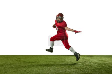 Foto de Hombre, jugador de fútbol americano en uniforme rojo atrapando pelota y corriendo en el campo contra fondo blanco. Concepto de deporte profesional, acción, estilo de vida, competencia, hobby, entrenamiento, anuncio - Imagen libre de derechos