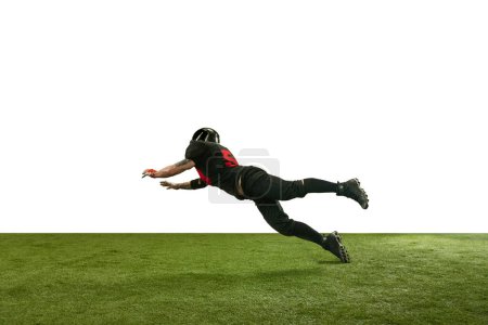 Foto de Imagen dinámica del hombre en uniforme negro y casco, jugador de fútbol americano en movimiento durante el juego cayendo sobre fondo blanco. Deporte profesional, acción, estilo de vida, competencia, entrenamiento, anuncio - Imagen libre de derechos